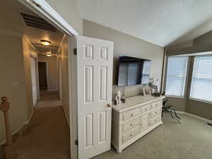 Corridor featuring a textured ceiling, light carpet, lofted ceiling, and an office area