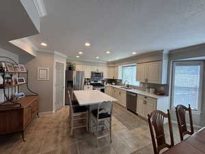 Kitchen with recessed lighting, appliances with stainless steel finishes, light countertops, a kitchen island, and a kitchen bar