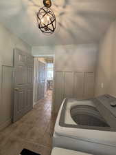 Interior space with washer / dryer, a textured ceiling, tile patterned flooring, a decorative wall, and a chandelier