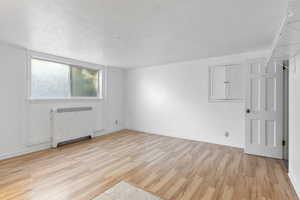 Empty room with radiator, light wood-style floors, and a textured ceiling