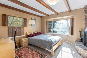 Carpeted bedroom with beam ceiling and a fireplace