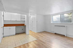 Interior space with radiator, white cabinets, light wood-style floors, open shelves, and a textured ceiling