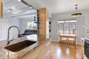 Kitchen with hanging light fixtures, light wood-style floors, light brown cabinets, black range with electric cooktop, and beamed ceiling