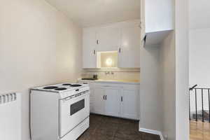 Kitchen with tile countertops, white electric range, white cabinetry, and tasteful backsplash