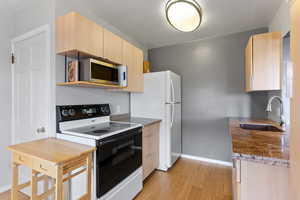 Kitchen featuring white electric stove, light brown cabinetry, light wood finished floors, and stainless steel microwave