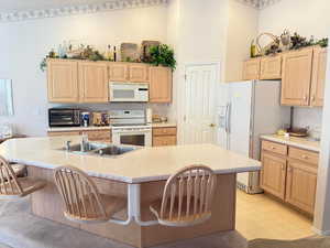 Kitchen with light countertops, white appliances, light brown cabinets, and a breakfast bar