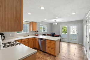 Kitchen with a peninsula, light countertops, decorative light fixtures, stainless steel dishwasher, and a chandelier
