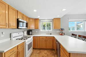 Kitchen with appliances with stainless steel finishes, a peninsula, light countertops, a breakfast bar, and recessed lighting