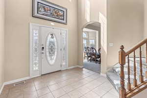 Entryway with arched walkways, a towering ceiling, light tile patterned floors, and stairs