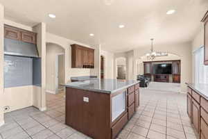 Kitchen with light tile patterned floors, under cabinet range hood, dark stone counters, and recessed lighting