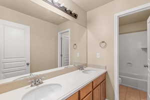 Full bathroom with light tile patterned floors, double vanity, and washtub / shower combination