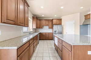 Kitchen with light stone countertops, brown cabinetry, light tile patterned flooring, tasteful backsplash, and recessed lighting