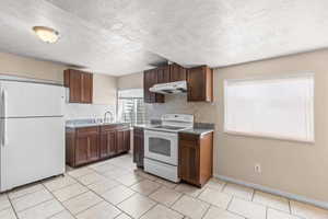 Kitchen with white appliances, a textured ceiling, light tile patterned floors, tasteful backsplash, and under cabinet range hood