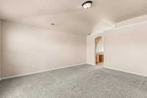 Unfurnished room with carpet flooring, vaulted ceiling, and arched walkways