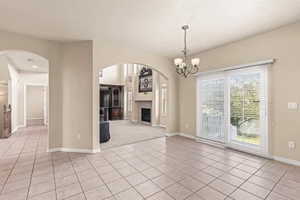 Unfurnished living room featuring a fireplace, light tile patterned floors, a chandelier, and arched walkways