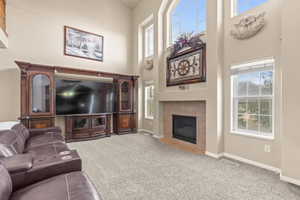 Carpeted living room featuring plenty of natural light, a towering ceiling, and a fireplace