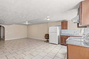 Kitchen featuring white appliances, brown cabinetry, tasteful backsplash, a textured ceiling, and arched walkways
