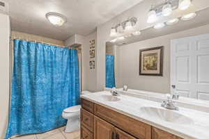 Bathroom with a textured ceiling, double vanity, light tile patterned flooring, and a shower with curtain