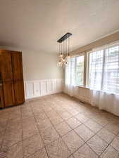Unfurnished dining area with a decorative wall, a wainscoted wall, and a textured ceiling