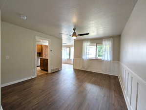Empty room featuring dark wood finished floors, a textured ceiling, a decorative wall, a ceiling fan, and a wainscoted wall