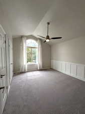 Carpeted spare room with lofted ceiling, a textured ceiling, a wainscoted wall, and a decorative wall