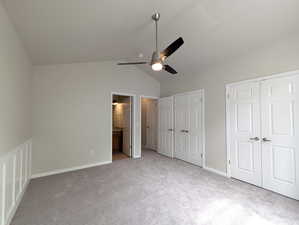 Unfurnished bedroom with vaulted ceiling, multiple closets, ensuite bathroom, carpet floors, and a ceiling fan