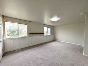 Empty room with a textured ceiling, light colored carpet, and a smoke detector