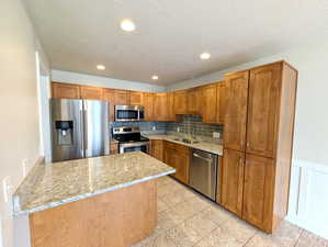 Kitchen with brown cabinets, appliances with stainless steel finishes, light stone counters, tasteful backsplash, and recessed lighting