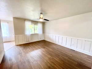 Spare room with a textured ceiling, a decorative wall, wainscoting, wood finished floors, and a ceiling fan