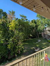 View of grassy yard featuring a balcony and view of scattered trees