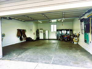 Garage with white fridge with ice dispenser, stainless steel fridge with ice dispenser, and a garage door opener