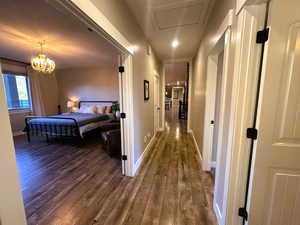 Hall featuring dark wood-style floors, a chandelier, and attic access