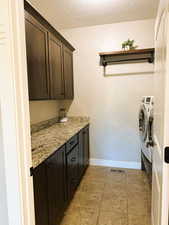 Laundry area with a textured ceiling, light tile patterned floors, and cabinet space