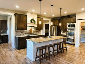Kitchen featuring dark brown cabinetry, a kitchen bar, decorative backsplash, stainless steel appliances, and light stone counters
