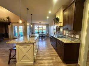 Kitchen with light stone counters, dark brown cabinetry, a breakfast bar, hanging light fixtures, and decorative backsplash