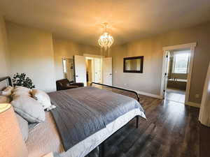 Bedroom with dark wood-type flooring, a chandelier, a textured ceiling, and ensuite bathroom