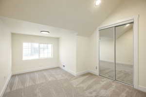 Unfurnished bedroom with light colored carpet, a textured ceiling, a closet, and lofted ceiling