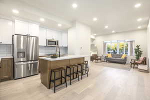 Kitchen featuring stainless steel appliances, recessed lighting, white cabinetry, brown cabinetry, and a kitchen island with sink