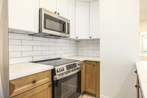 Kitchen with stainless steel appliances, decorative backsplash, white cabinetry, and brown cabinets