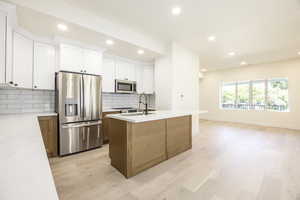 Kitchen with brown cabinetry, stainless steel appliances, recessed lighting, tasteful backsplash, and white cabinetry
