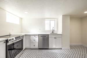Kitchen with appliances with stainless steel finishes, healthy amount of natural light, white cabinets, a textured ceiling, and light stone countertops