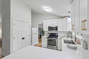 Kitchen featuring stainless steel appliances, lofted ceiling, white cabinets, hanging light fixtures, and light wood-style floors