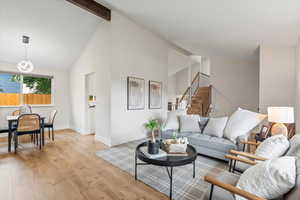 Living room featuring wood finished floors, high vaulted ceiling, beam ceiling, and stairs