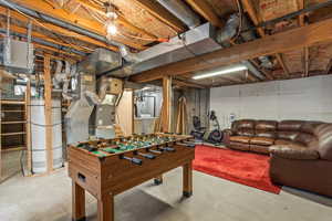 Rec room with unfinished concrete floors, water heater, washer / dryer, and heating unit