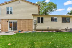 Rear view of house with brick siding, a lawn, and a patio
