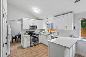 Kitchen featuring appliances with stainless steel finishes, vaulted ceiling, light wood-type flooring, white cabinetry, and a peninsula