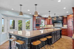 Kitchen featuring a kitchen bar, glass insert cabinets, light stone counters, decorative backsplash, and recessed lighting