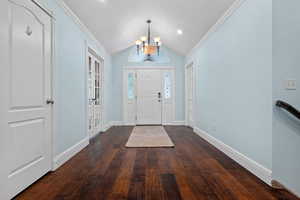 Entrance foyer featuring lofted ceiling, a chandelier, dark wood-style flooring, crown molding, and french doors