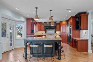 Kitchen featuring tasteful backsplash, hanging light fixtures, light tile patterned floors, a kitchen bar, and light stone counters