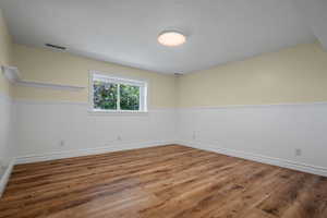 Empty room featuring wainscoting, wood finished floors, and a textured ceiling